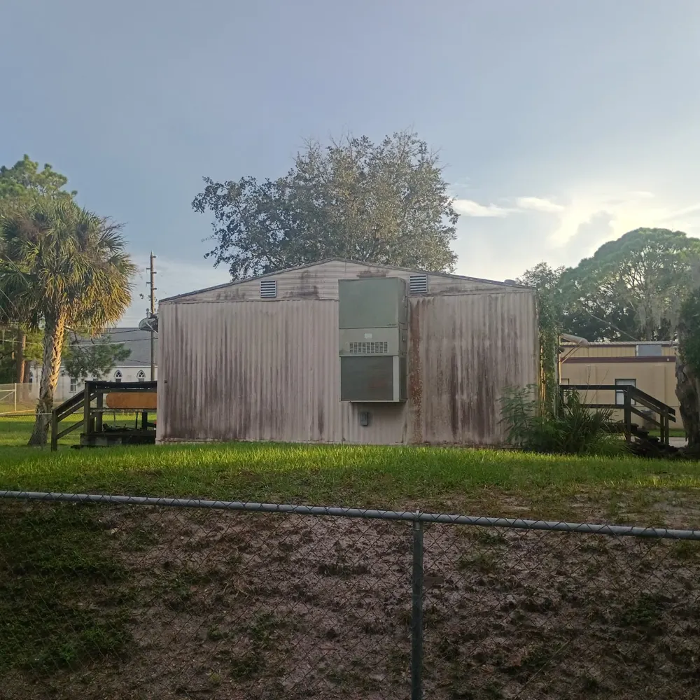 Side of the building facing Old Tampa Highway, with heavy staining on the siding and a wall-mounted air conditioning unit